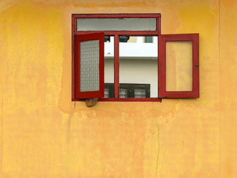 Red old grunge window in yellow house facade