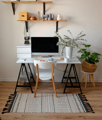 A chic workplace in Scandinavian style. White chair, on the computer table and eucalyptus in a white pot. Wooden shelves with home decor.