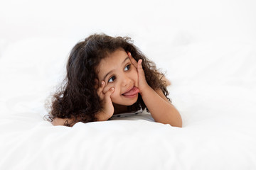 Funny little girl lying on stomach on bed making funny face