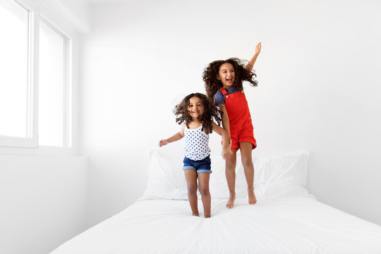 Happy sisters wildly jumping on bed