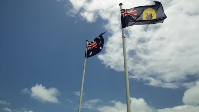 Flag of Western Australia with the Australian flag above the HMAS Sydney II Memorial in Geraldton against blue cloudy sky, atop Mount Scott overlooking the city in Western Australia.