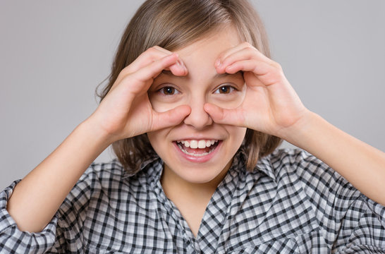 Close-up emotional portrait of caucasian little girl. Funny kid making binoculars using her hands, on gray background. Beautiful child laughing looking very happy.