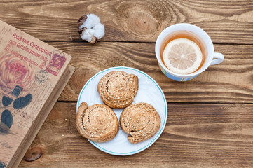 Tea with lemon, homemade cookies and a book on a wooden table.