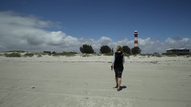 Carefree woman walking on white beach with dunes of Geraldton, Western Australia. The historic Moore Lighthouse Point built in 1878, is an icon of Geraldton. Australia travel freedom concept.