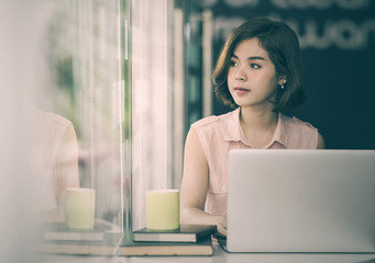 Beautiful asian woman sitting at desk and using laptop while looking outside