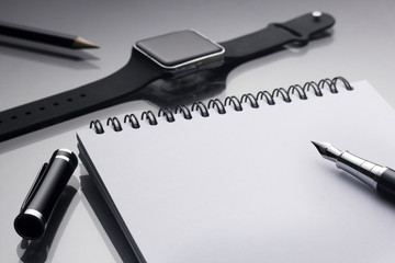 White notepad on it black pen near a smart clock and pencil closeup on a glossy desk, concept