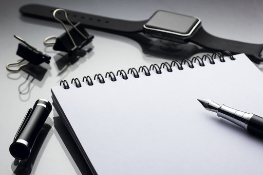 White notepad on it black pen near a smart clock closeup on a glossy desk, concept