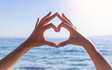 Hands in the shape of heart against the background of the sea.