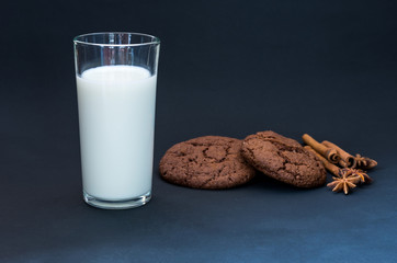 A glass of milk and chocolate gingerbread with cinnamon stickers.