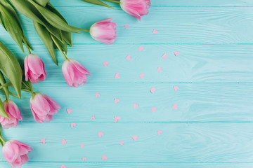 Pink tulips bouquet and paper hearts on blue wooden background, copy space and flat lay.