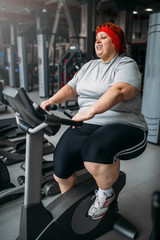 Fat woman training on exercise bike in gym