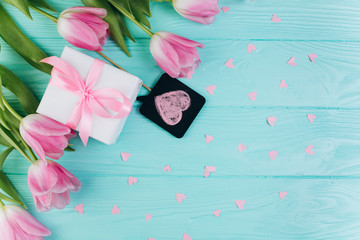 Pink tulips, gift and paper hearts on blue wooden background, copy space and flat lay. Mother's Day concept.
