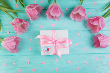 Pink tulips, gift and paper hearts on blue wooden background, copy space and flat lay. Mother's Day concept.