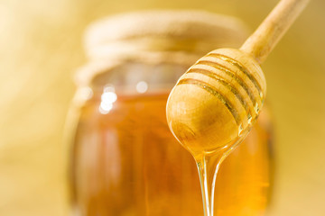 A honey spoon against the background of a jar filled with honey