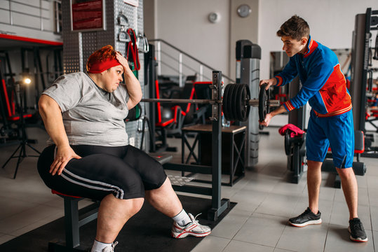 Fat woman using barbell, training with instructor
