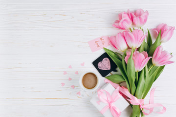 Obraz na płótnie Canvas Pink tulips, gift, cup of coffee and paper hearts on white wooden background, copy space and flat lay. Mother's Day concept.