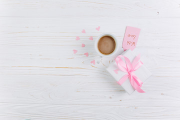Gift, cup of coffee and paper hearts on a white wooden background, copy space and flat lay. Valentines Day and Mother's Day concept.