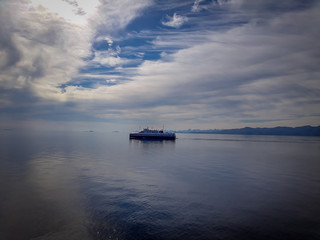 ferry sailing in the middle of the calm norwegian fjord, against the backdrop of a blue sky with white clouds reflecting on the water