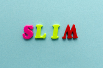 word 'slim' from plastic colored magnet letters on blue paper background