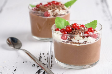Chocolate mousse with currant and mint in a glasses on a whiite wooden background.