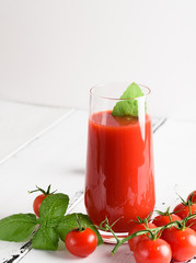 Tomato juice in a glass with a cherry and basil on a light background