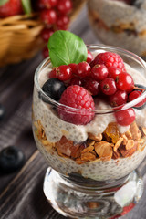 Two glasses of chia pudding with fresh strawberries, raspberries and blueberries. Basket with berries. On a wooden grey background.