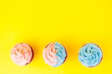 Cupcake red velvet with blue and pink whipped cream on yellow background. Picture for a menu or a confectionery catalog. Top view.