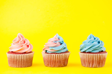 Cupcake red velvet with blue and pink whipped cream on yellow background. Picture for a menu or a confectionery catalog. Top view.