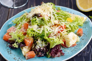 Fresh smoked salmon salad with lettuce leaves, parmesan cheese and rusks served with lemon slice, close up. Healthy food