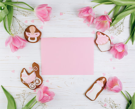 A composition for newborns on a wooden white background with pink tulips, hearts and a cookies, copy space and flat lay. It's a girl.