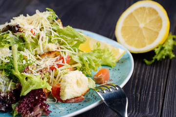 Fresh smoked salmon salad with lettuce leaves, parmesan cheese and rusks served with lemon slice, close up. Healthy food