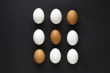 Set of fresh chicken egg in container on black paper background. Concept for Easter with copy space. Creative layout made of white and brown eggs. Top view photo.