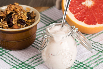 Jar with homemade yogurtGranola from several types of cereals with nuts, coconut shavings and dried cranberries. and grapefruit
