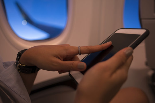 Closely image of a woman hands is holding cell telephone with empty screen background for your advertising content. Closeup of female is watching photos on mobile phone while flying in an airplane