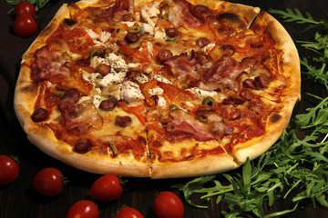Pizza with bacon, sausages, ham, tomato and olives. Sprinkle with arugula and served with tomato and cheese. Pizza Restaurant. Snack, dinner
