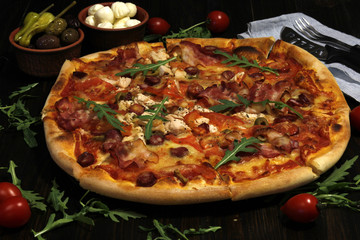 Obraz na płótnie Canvas Pizza with bacon, sausages, ham, tomato and olives. Sprinkle with arugula and served with tomato and cheese. Pizza Restaurant. Snack, dinner