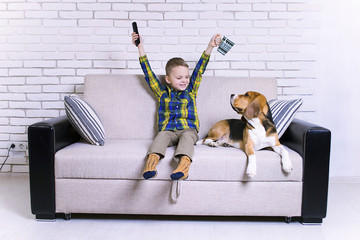 funny boy with remote control watching TV together with a dog on the couch