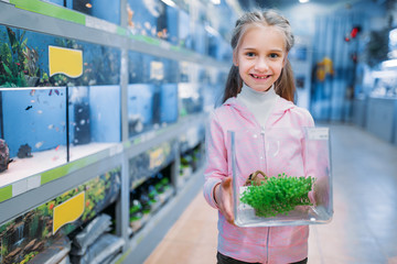 Little girl with plant for aquarium in pet shop