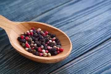 Mixed red, black,green and red peppercorn in wooden spoon on rustic plank background, copy space. Kitchen, cooking concept