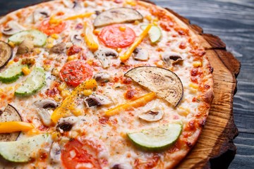 Delicious fresh vegetarian pizza with tomato, zucchini, eggplant, olives and mushrooms served on wood, selective focus