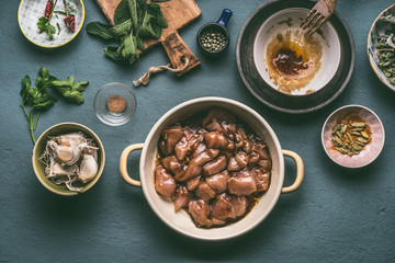 Pot with marinated chicken breast  pieces on kitchen table background with bowls ingredients, top view. Dieting cooking eating and healthy food concept