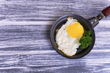 fried egg in a frying pan with greens on a wooden background