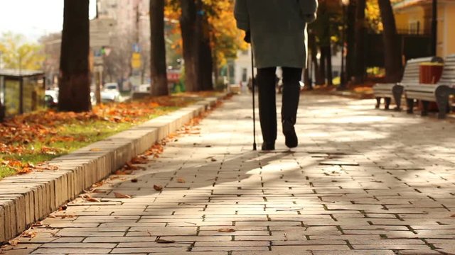 Lonely, old, person walking down street with stick, limping. Gait, legs disease