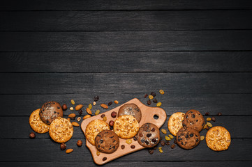 Freshly baked cookies on a wooden table. On the table is a plank, around various nuts, almonds and raisins.