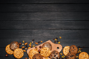 Freshly baked cookies on a wooden table. On the table is a plank, around various nuts, almonds and raisins.