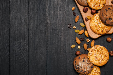 Freshly baked cookies on a wooden table. Lies on a wooden reach, around different nuts, almonds and raisins.