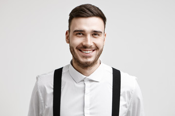 Positive human facial expressions, emotions, feelings and life perception. Isolated studio shot of handsome cheerful young male employee with trendy hairstyle and trimmed beard smiling cheerfully