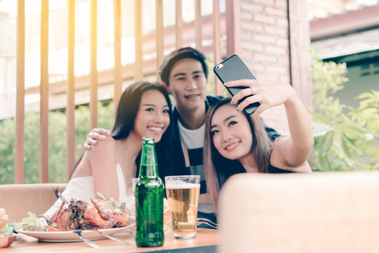 Group of asian smiling friends taking selfie in restaurant.