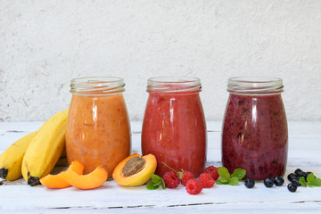 Orange, red and purple smoothies of fresh ingredients - bananas, apricots, raspberries and blueberries on a light background. Healthy food concept. Vegetarian product. Organic Raw Drink. Copy space.