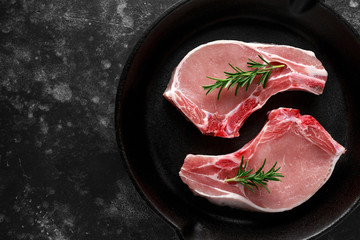 Raw Pork Loin chops in rustic skillet, pan with rosemary. top view. background
